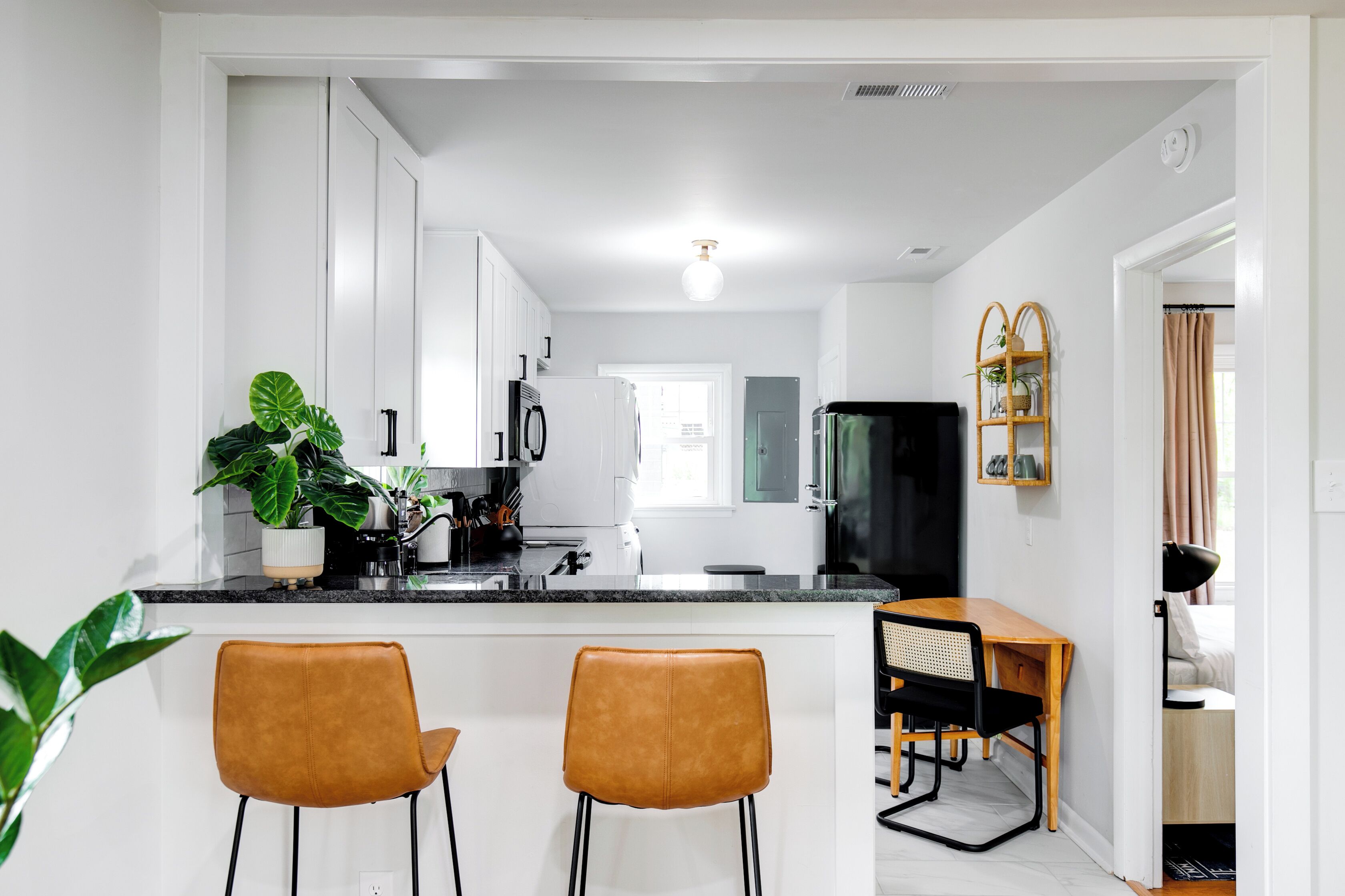 A modern kitchen with white cabinets, a black refrigerator, and a wooden dining table with two chairs.
