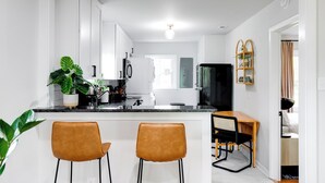 A modern kitchen with white cabinets, a black refrigerator, and a wooden dining table with two chairs.