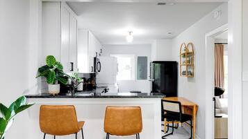 A modern kitchen with white cabinets, a black refrigerator, and a wooden dining table with two chairs.
