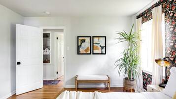 A bedroom with a bed, a bench, a potted plant, and two framed artworks on the wall.