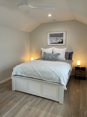 A bedroom with a bed, bedside lamps, a framed picture on the wall, and a ceiling fan. - Bryon's secret hideout studio (Byron Bay)