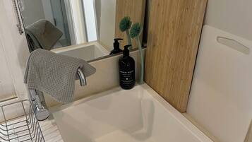 Une salle de bain avec un lavabo blanc, un miroir, un panneau en bois, une bouteille noire et un porte-serviettes.