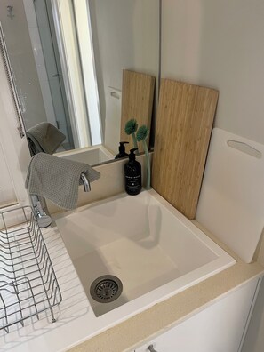 A bathroom with a white sink, a mirror, a wooden panel, a black bottle, and a towel rack. - Bryon's secret hideout studio (Byron Bay)