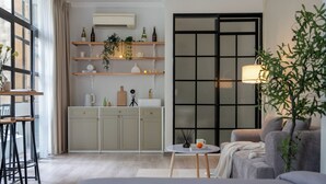 Uma sala de estar moderna com um sofá cinzento, uma mesa de centro redonda e uma janela ampla com vista para a cidade.