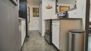 Une cuisine étroite avec des meubles blancs, une poubelle en acier inoxydable et une cuisinière.