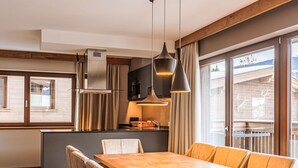 Une cuisine moderne dotée d’un îlot central, de luminaires suspendus et de grandes fenêtres offrant une vue sur l’extérieur.