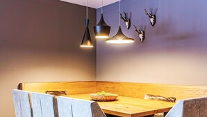 Un espace repas moderne avec un banc en bois, des chaises à revêtement gris et des luminaires suspendus.