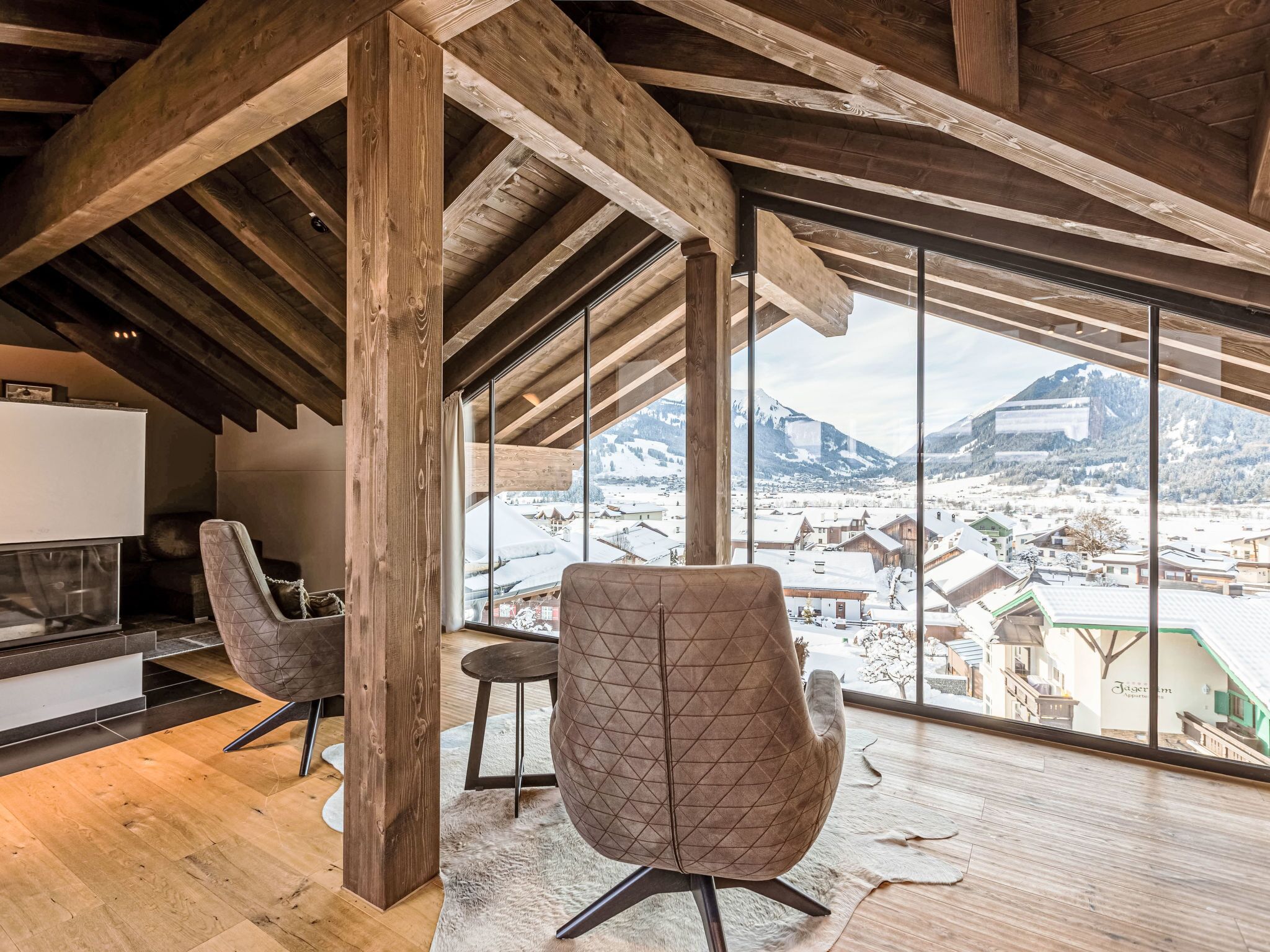 Een ruime kamer met een hoge plafond en houten balken, met een groot raam en uitzicht op een besneeuwde berg.