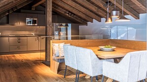 Eine moderne Küche mit Holzbalken, ein Essbereich mit Holztisch und -stühlen und Blick ins Freie.