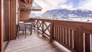 Eine Holzterrasse mit Tisch und Stühlen, mit Blick auf eine verschneite Berglandschaft.