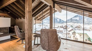 A spacious room with a high ceiling and wooden beams, featuring a large window with a snowy mountain view.