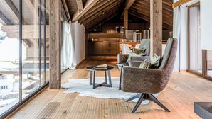 A spacious loft with a high ceiling, wooden beams, a large window, and a cozy seating area with a rug and a table.