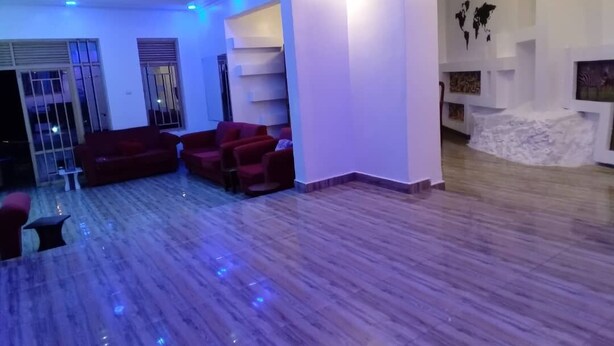 A spacious living area with a wooden floor, red sofas, and a white reception desk. - Queen Greenstars Apartment  (Gisenyi)