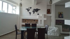 A dining area with a glass table and chairs, a world map on the wall, and artwork on shelves. - Queen Greenstars Apartment  (Gisenyi)