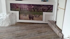 A room with a wooden floor, a white reception desk, two pendant lights, and a zebra mural. - Queen Greenstars Apartment  (Gisenyi)