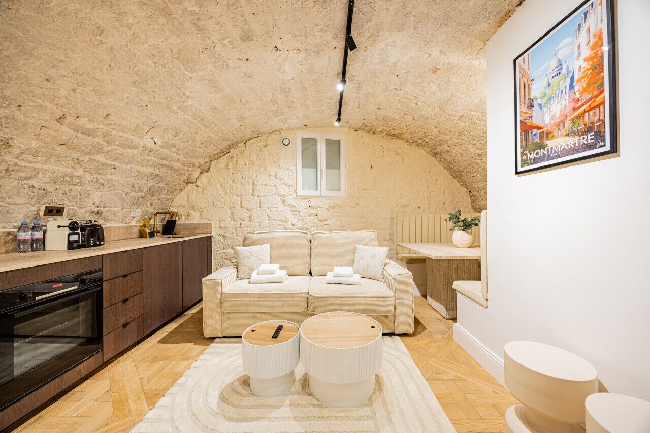 Een gezellige kamer met een stenen plafond, een kitchenette, een zithoek en een ingelijst schilderij aan de muur.