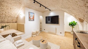 Quarto moderno estilo loft com teto abobadado, uma televisão de tela grande, um espaço de estar aconchegante com almofadas e uma pequena mesa de jantar.