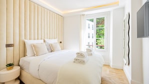 Quarto de hotel moderno com uma cama grande, uma mesa de cabeceira com uma planta e vista para o verde lá fora.