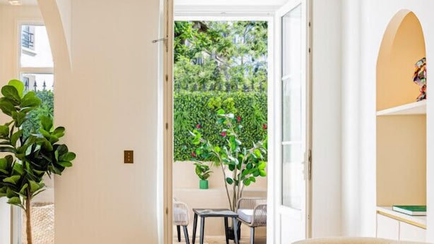 Uma sala de estar moderna com um sofá bege, uma mesa de centro de madeira e vista para um jardim através de uma porta aberta.