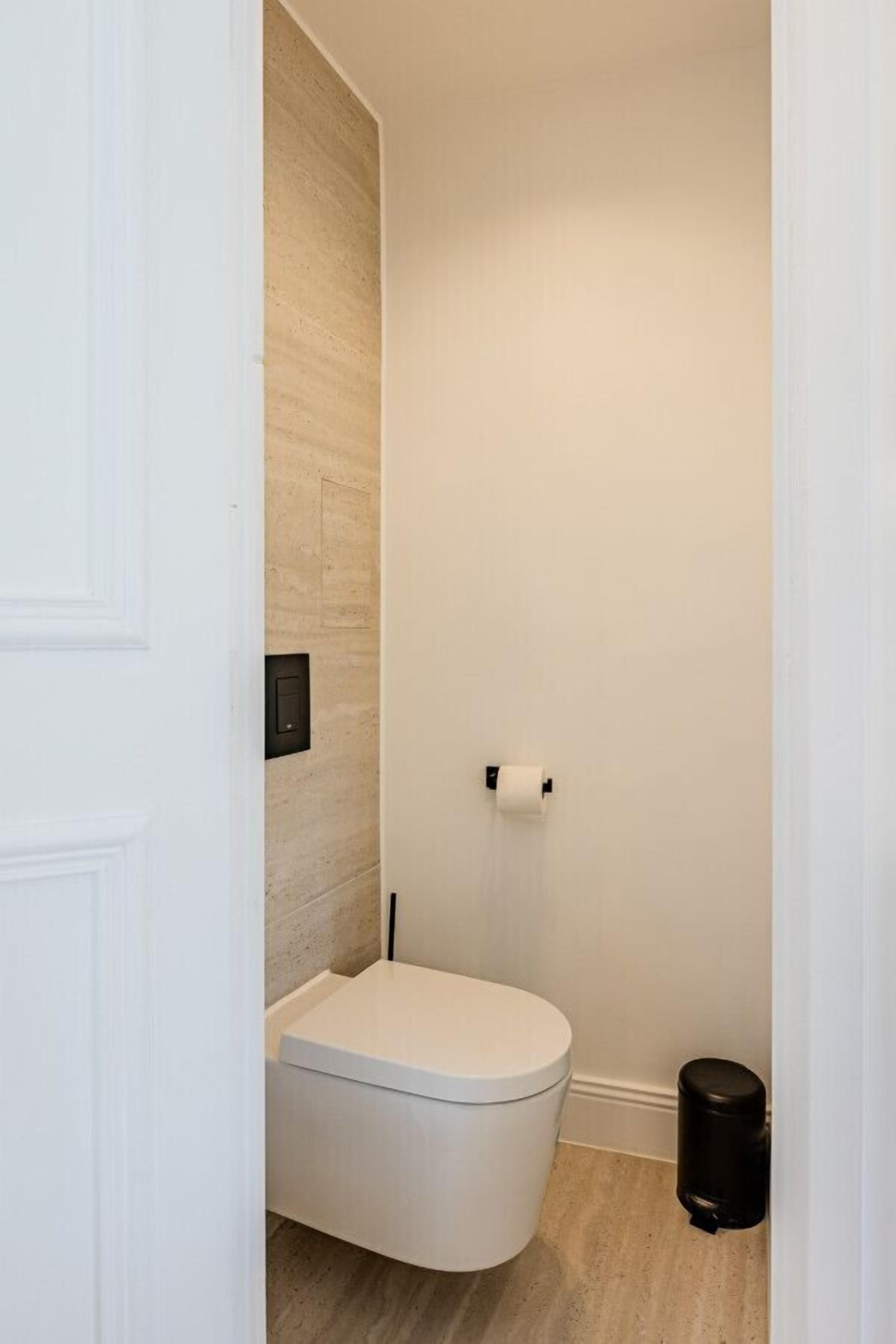 Une petite salle de bain moderne avec des toilettes blanches, un mécanisme de chasse d'eau mural et une poubelle noire.