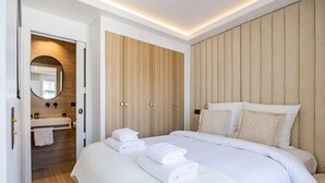 Moderni hotellihuone, jossa on suuri sänky, puinen vaatekaappi, peilillä varustettu kylpyhuone ja pyyheteline.