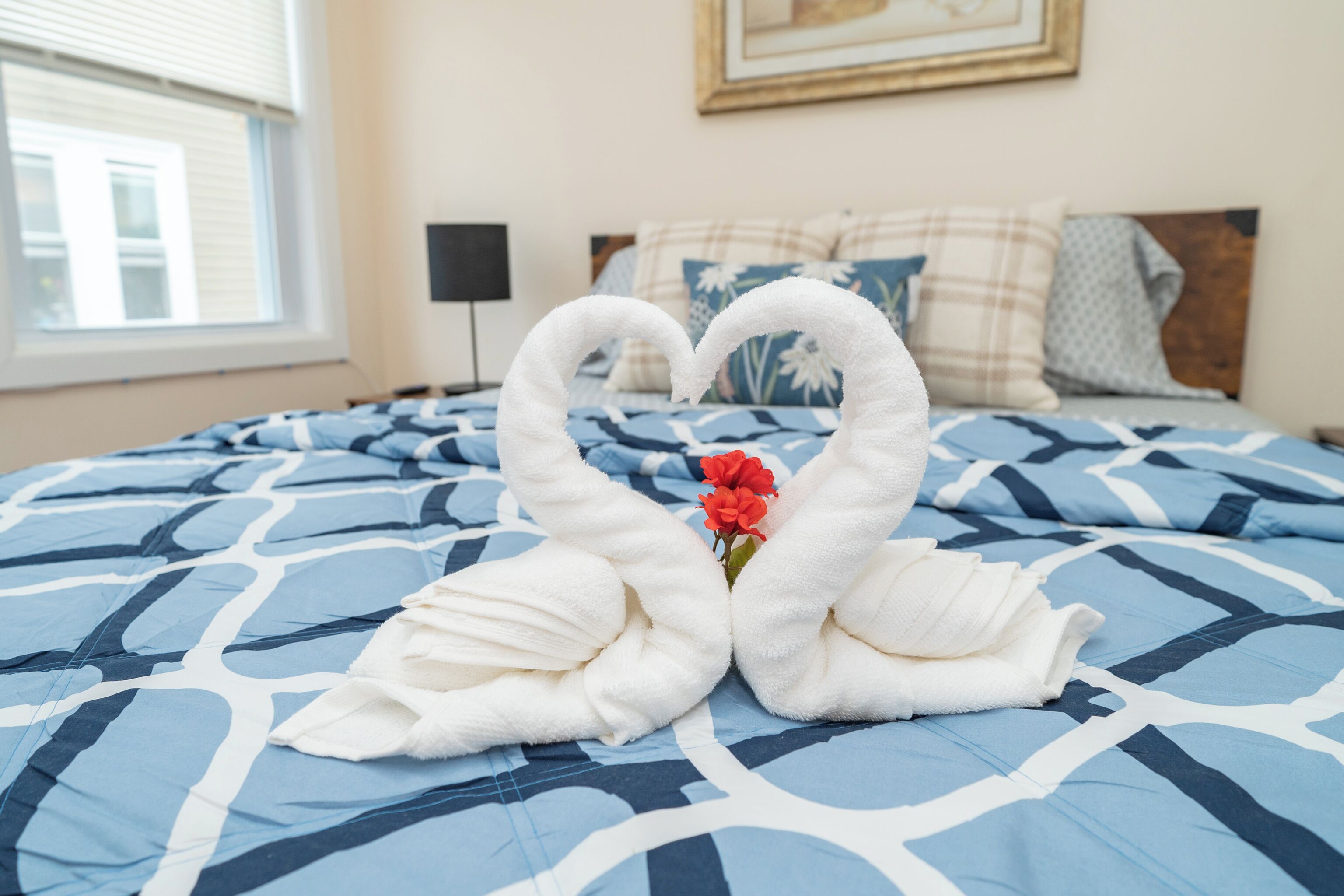 Un lit recouvert d’une couvre-lit à motifs bleus et blancs, une serviette pliée en forme de cœur et une seule fleur rouge.