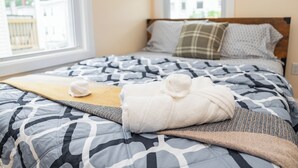 Una cama bien tendida con una colcha estampada, una toalla blanca enrollada y un plaid marrón.