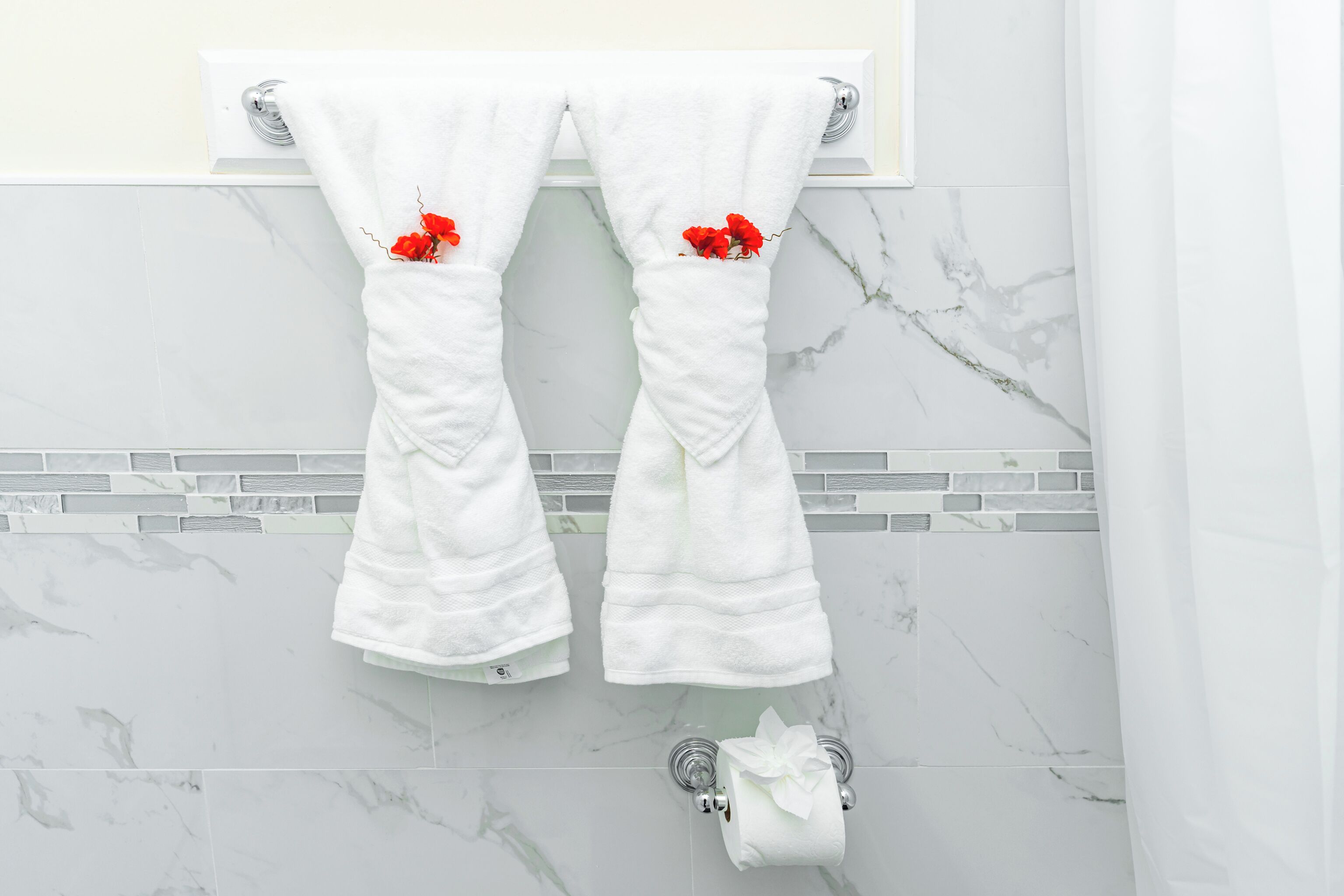 Casa de banho com azulejos de mármore branco, um porta-toalhas branco com duas toalhas e um rolo de papel higiénico.