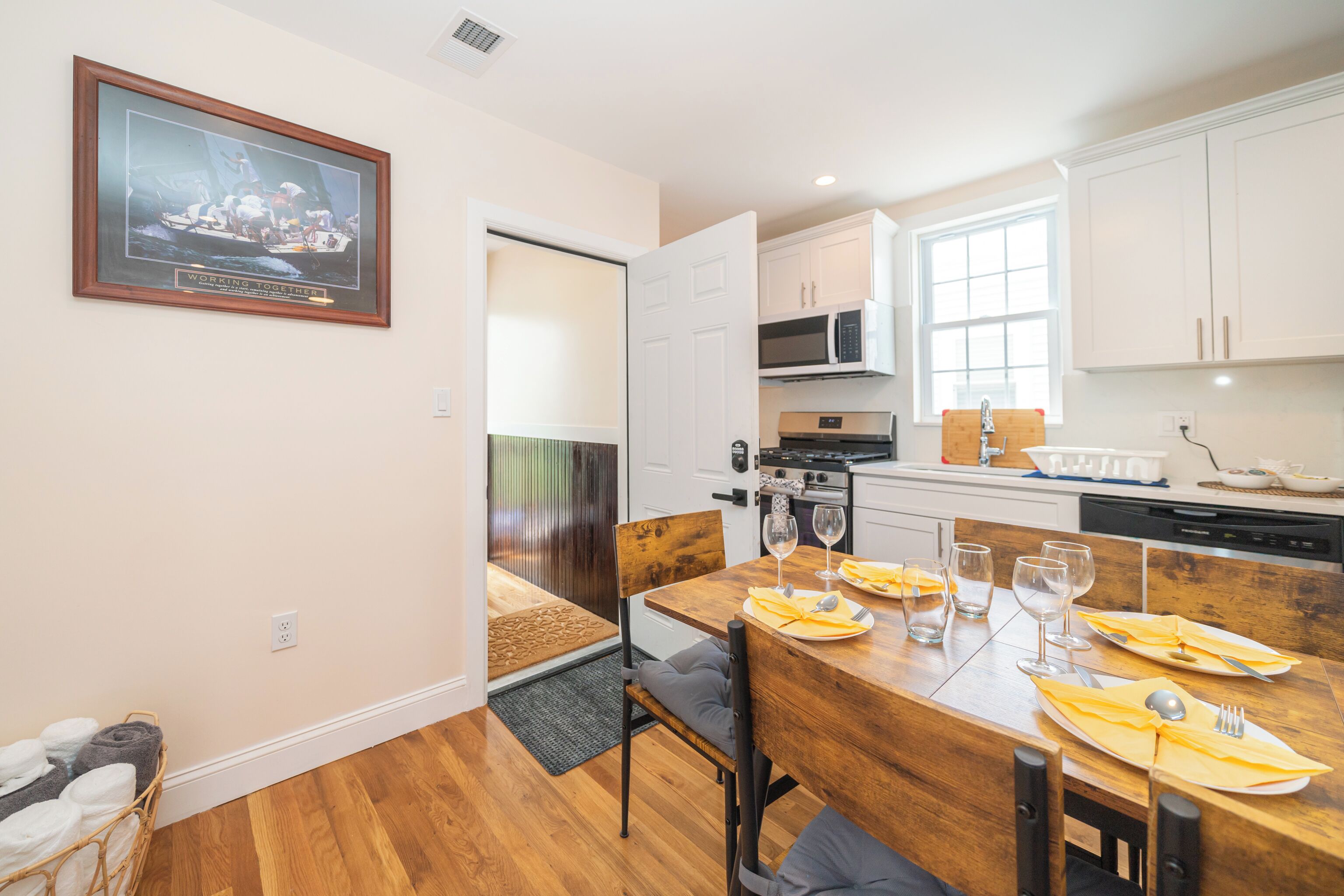 Une cuisine moderne avec des meubles blancs, une table à manger dressée pour quatre personnes et un tableau encadré accroché au mur.