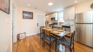Una cocina moderna con armarios blancos, electrodomésticos de acero inoxidable y un comedor con mesa y sillas de madera.