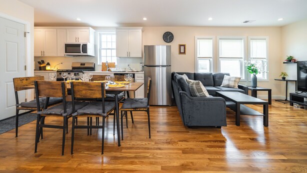Una cocina moderna con armarios blancos, un refrigerador de acero inoxidable y un comedor con mesa y sillas de madera.