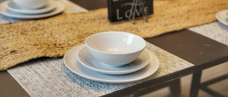 A table with white bowls and plates, a woven placemat, and a sign that says "LIVE LAUGH LOVE".