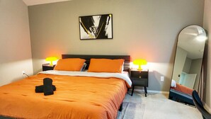 Un lit bien fait, avec une couvre-lit orange et deux oreillers, un grand miroir et deux lampes de chevet.
