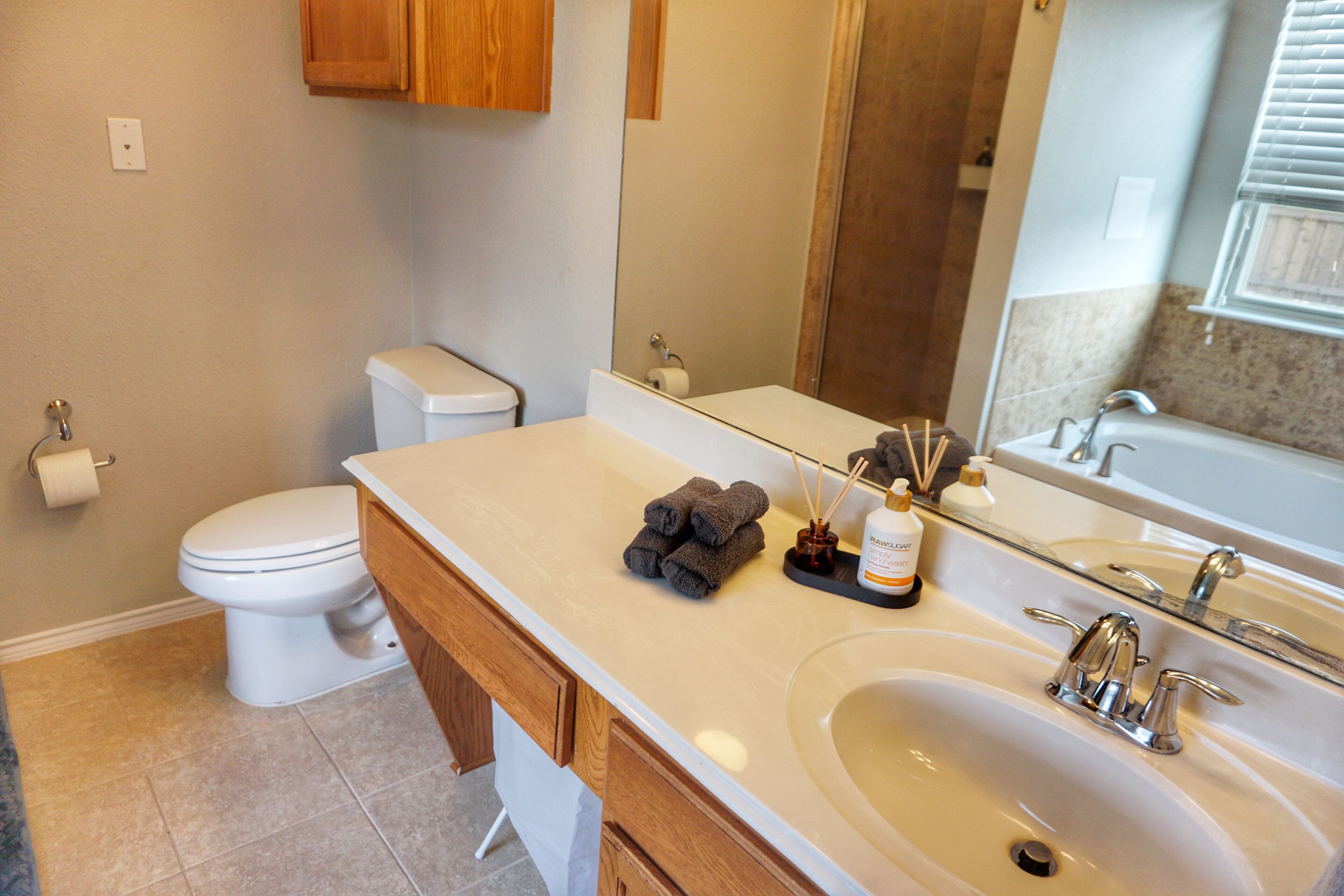 A bathroom with a toilet, sink, mirror, and wooden cabinets.