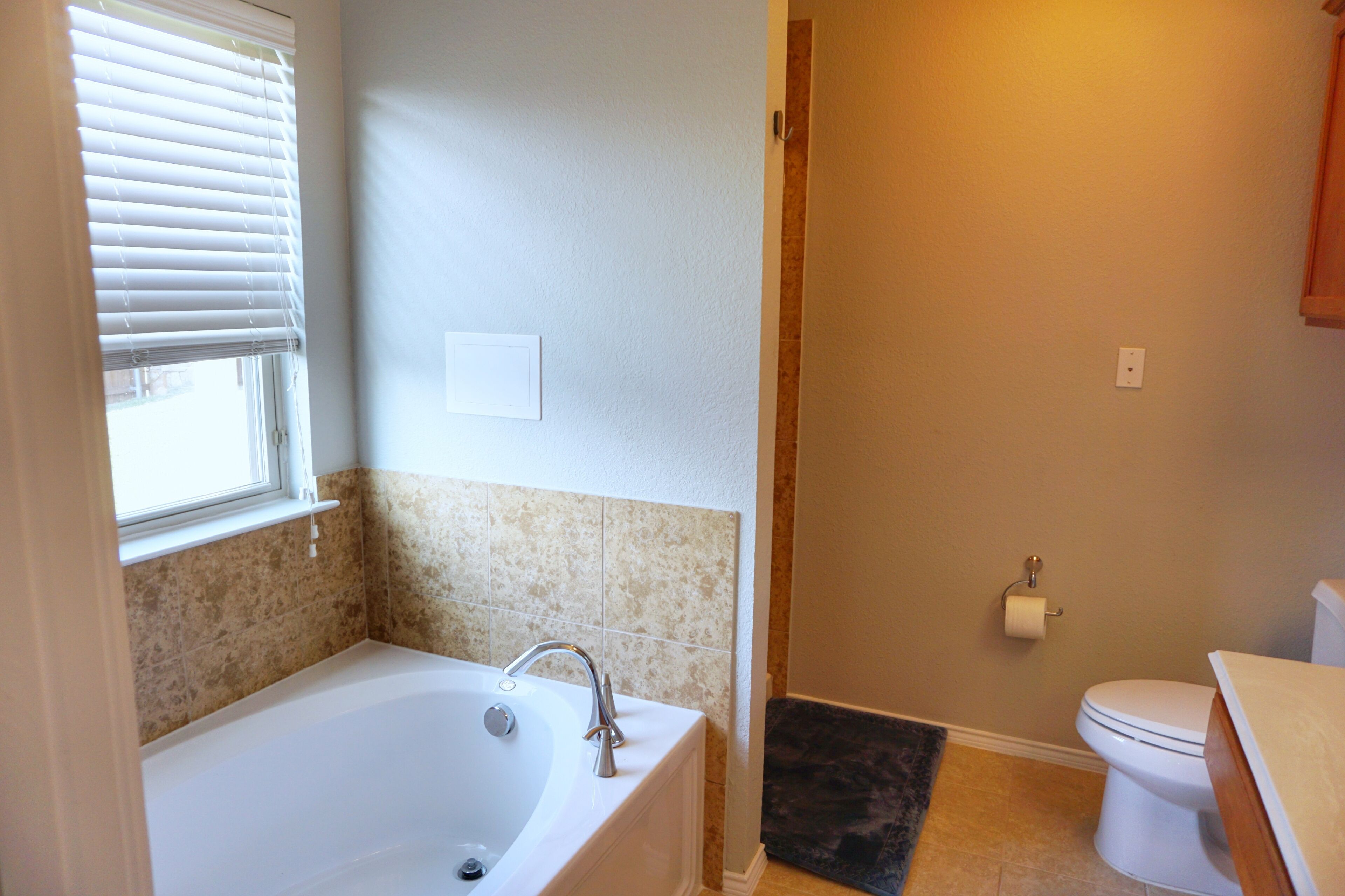 A bathroom with a bathtub, toilet, and a window with blinds.