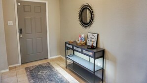 Un couloir avec une porte grise, une console ornée de divers objets décoratifs et un miroir fixé au mur.