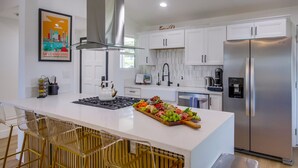 Une cuisine moderne avec des meubles blancs, un réfrigérateur en acier inoxydable et un îlot central doté de tabourets de bar.