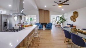 Une cuisine moderne avec un îlot central, un coin repas avec des chaises bleues et un espace de vie doté d’une cheminée.