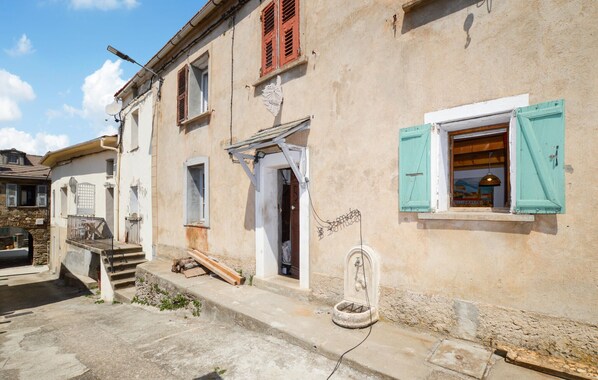 Una calle estrecha con un edificio que presenta un pequeño porche, una escalera de madera y una ventana con vistas coloridas.