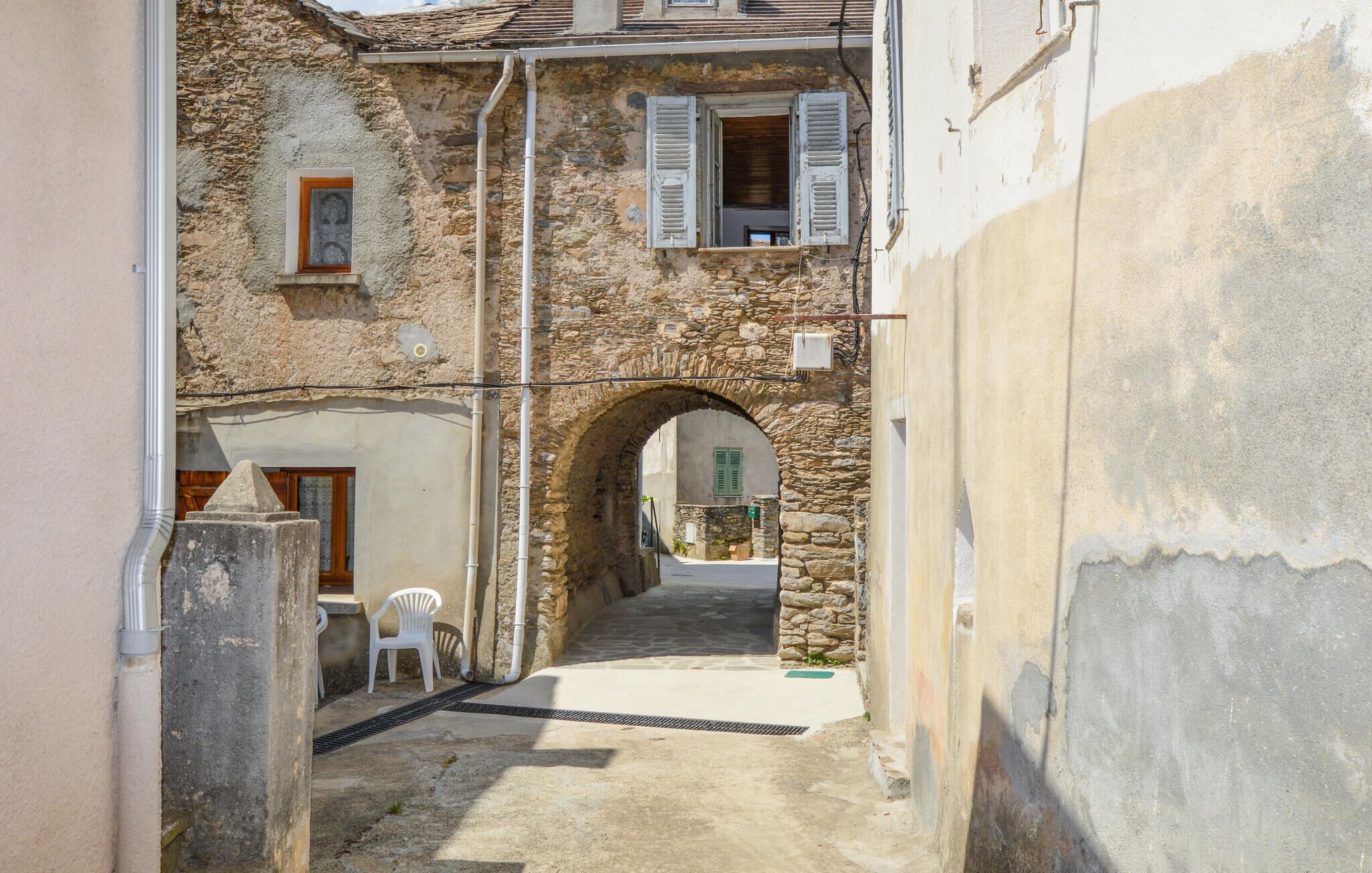 A narrow stone alleyway with an archway leading to a building with a wooden door and a window with shutters.