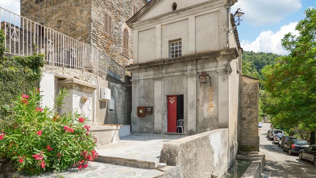 Un edificio de piedra con una puerta roja, un balcón pequeño y una calle con coches estacionados.