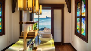 A bathroom with a large window offering a view of the ocean and a wooden ceiling. - Villa Zébra Moon by muse villas  (Bain Boeuf)