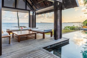 Eine Holzterrasse mit Liegestühlen und einem Tisch mit Blick auf einen Pool und den Ozean.