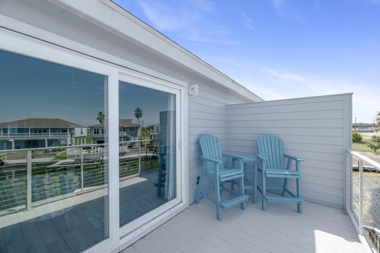 A balcony with two blue Adirondack chairs, a glass door, and a view of a marina.