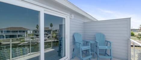 A balcony with two blue Adirondack chairs, a glass door, and a view of a marina.