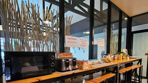 A modern kitchen with a microwave, toaster, and a coffee machine. There are wooden stools and a long counter. - Mercy Hostel (Chiang Rai)