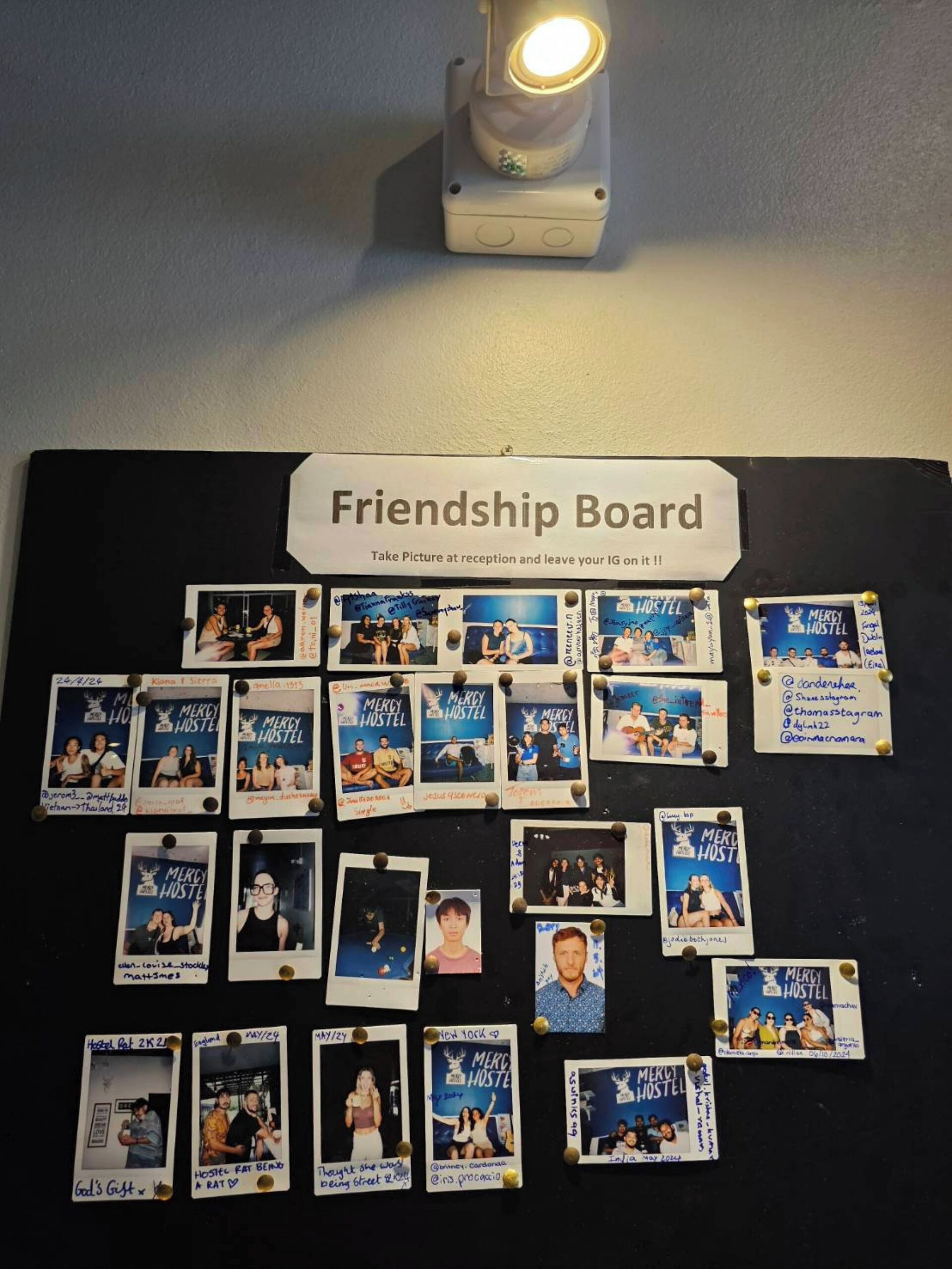 En opslagstavle med fastgjorte billeder og et skilt, der beder om at tage et billede i receptionen og hænge det på.