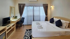 A hotel room with a bed, a desk with a chair, a television, and a window with curtains. - Mercy Hostel (Chiang Rai)