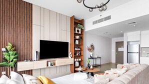 Un salon moderne avec un grand téléviseur à écran plat fixé au mur, une bibliothèque en bois, un canapé avec des coussins et une petite table ronde sur laquelle est posé un vase.