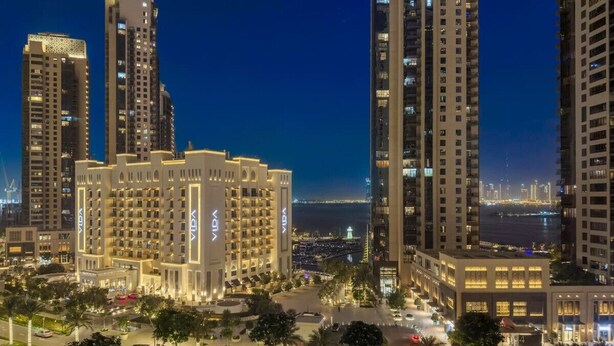 Un hôtel de grande hauteur, avec de nombreux étages, une piscine et une vue sur les toits de la ville illuminés la nuit.